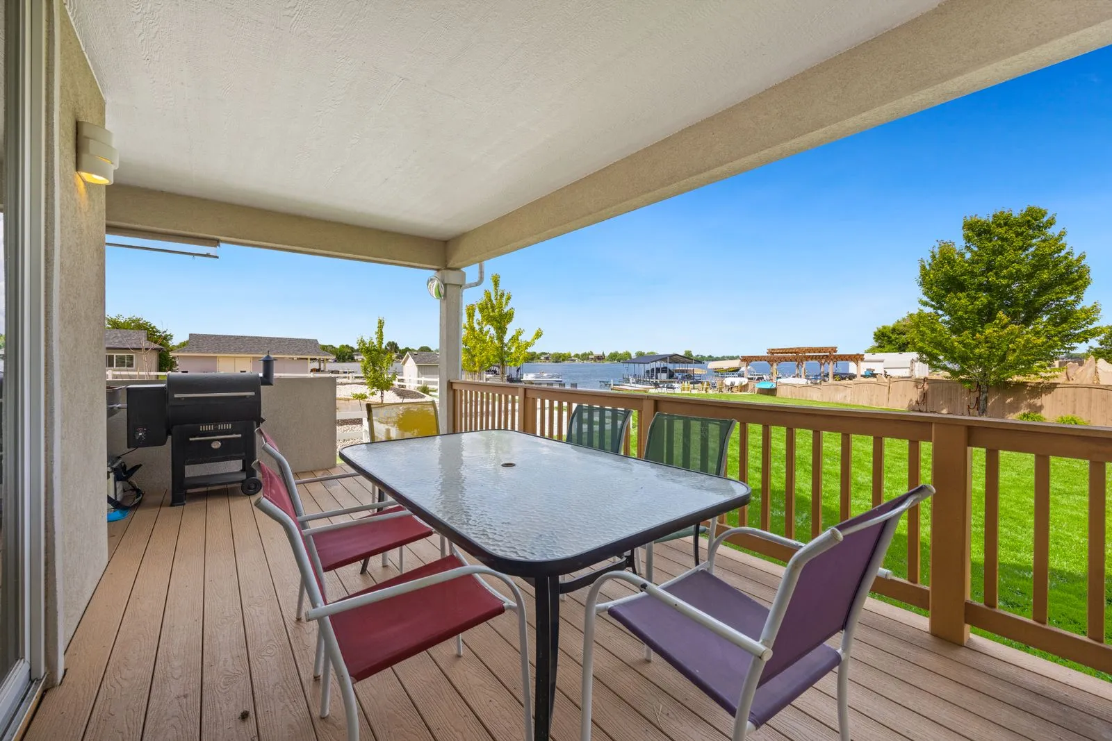 Spacious patio with outdoor seating and BBQ overlooking a serene lake on a sunny day.